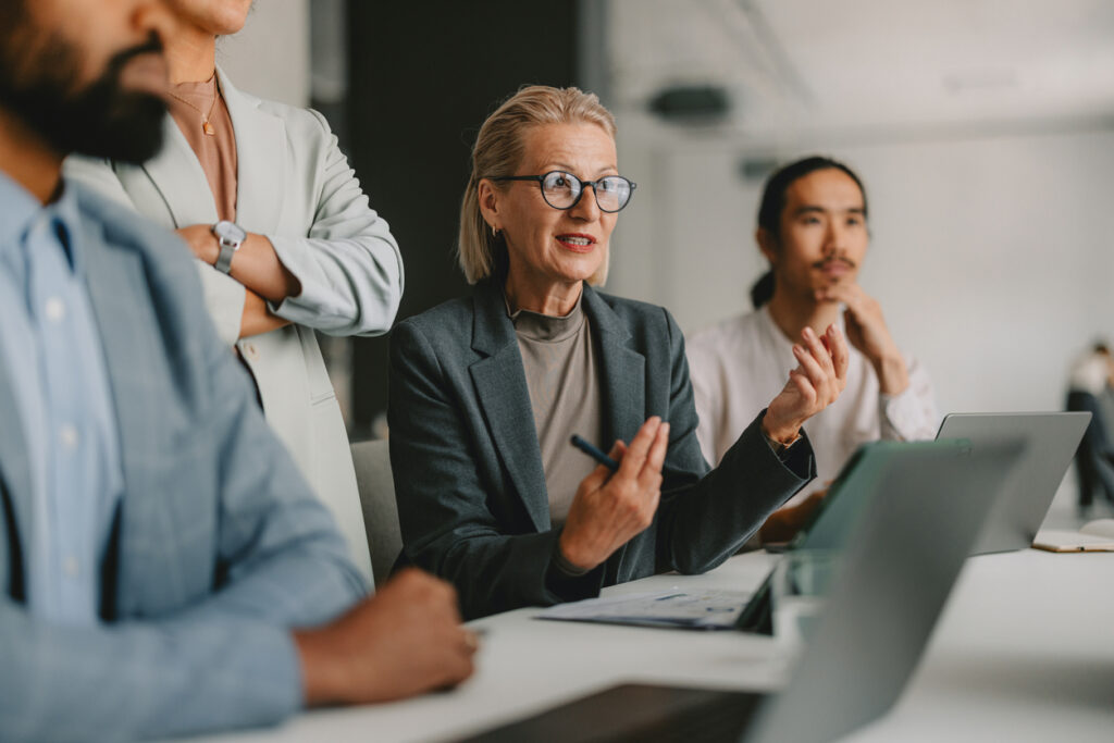 A diverse group of professional individuals engaged in a business meeting about intellectual property renewals within a bright beige office, illustrating teamwork, collaboration, and leadership.